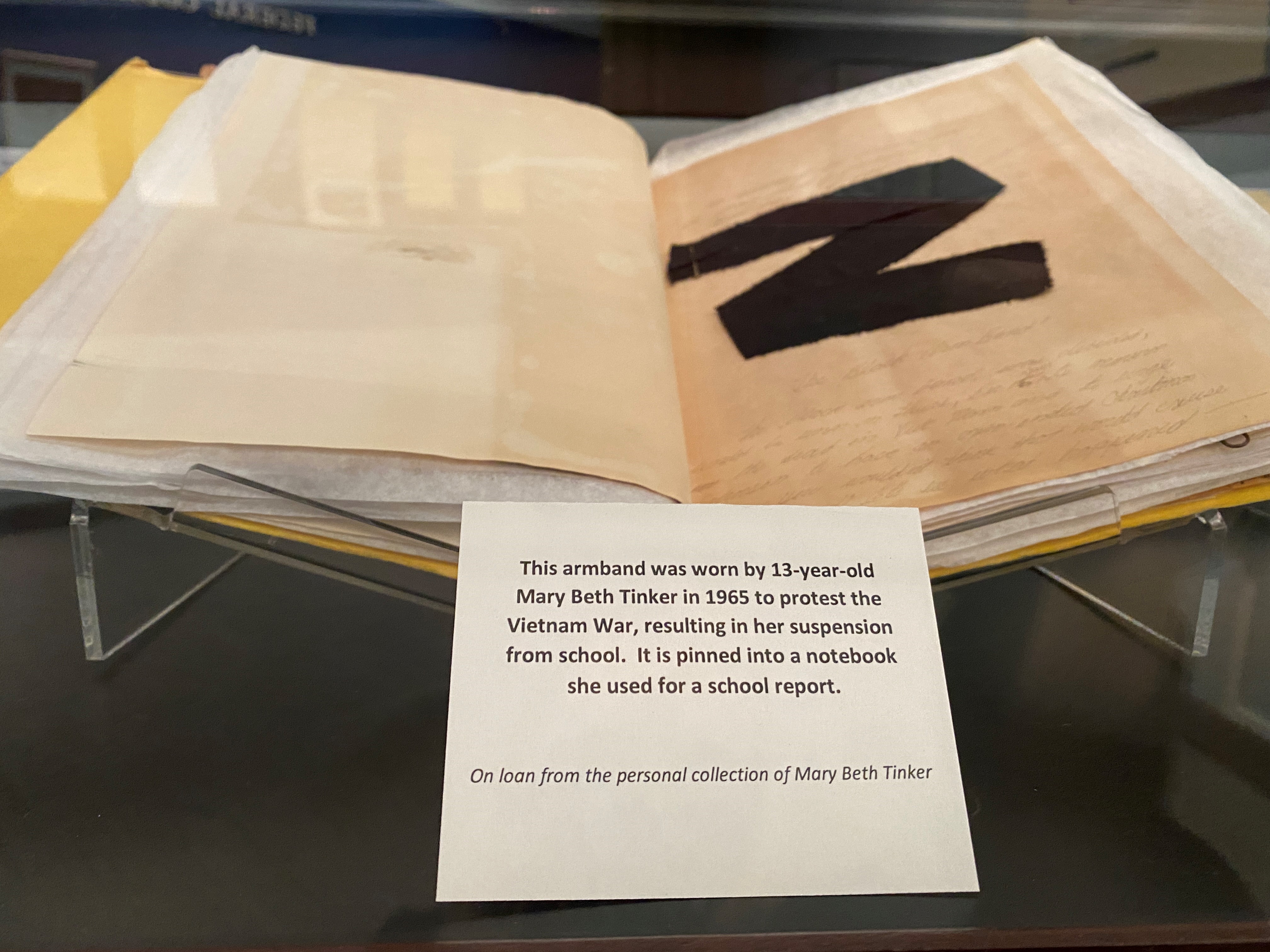 This armband was worn by 13-year-old Mary Beth Tinker in 1965 to protest the Vietnam War, resulting in her suspension from school. It is pinned into a notebook she used for a school report. On loan from the personal collection of Mary Beth Tinker.